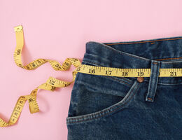 Measuring tape around the waist of an empty pair of jeans.