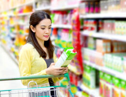 A woman in a grocery store reads the label on a carton