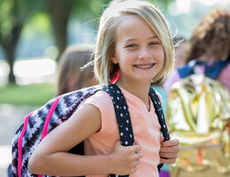 A girl wearing a backpack smiles.