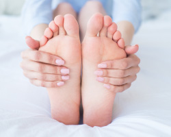 Close-up of manicured hands wrapped around the soles of bare feet