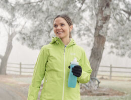 A woman carrying a water bottle walks outside on a foggy day. 