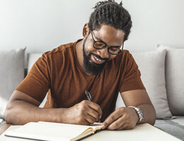 A smiling man writes in a journal.