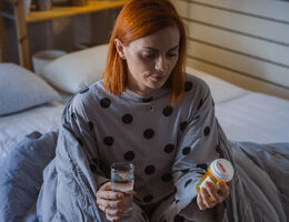 Woman sitting in bed and looking at a medicine bottle.