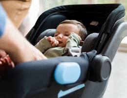 A baby in a car seat in a living room.